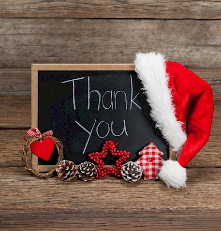 Chalk written on black board saying Thank You with a Santa hat placed on the top right hand corner of the black board